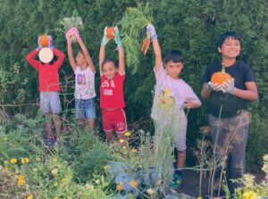Students holding up pumpkins and vegetables in the Garden